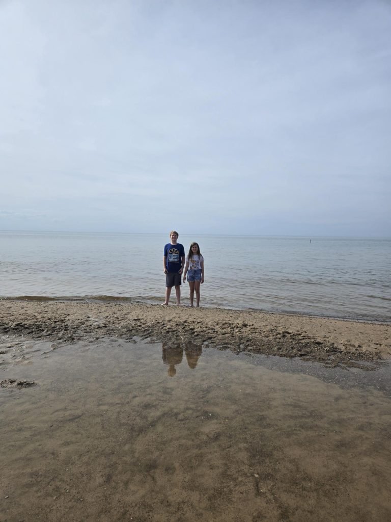 Two children, one boy and one girl, standing in the sand at the end of Lake Michigan on the beach at Indiana Dunes National Park.