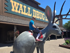 A boy sitting on a jackalope statue in front of Wall Drug in South Dakota