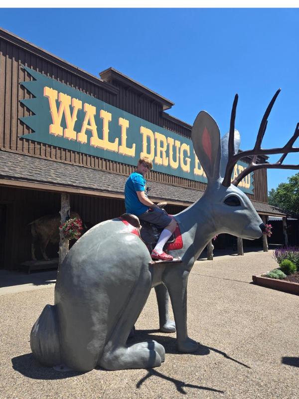 A boy sitting on a jackalope statue in front of Wall Drug in South Dakota